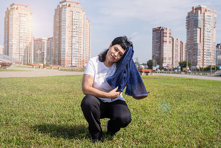 生活艰苦摄影照片_在公园户外艰苦锻炼后擦汗的老年妇女