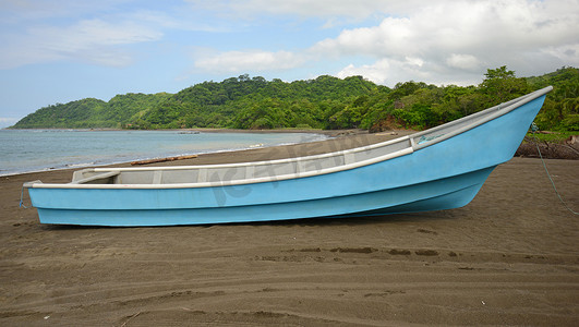 划船小船摄影照片_靠近海洋的海滩上的蓝色小船将热带雨林