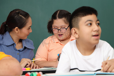 自闭症教育摄影照片_亚洲残疾儿童 或者，一名自闭症儿童在课桌前与老师一起学习阅读、写作和训练他们的手和手指肌肉。