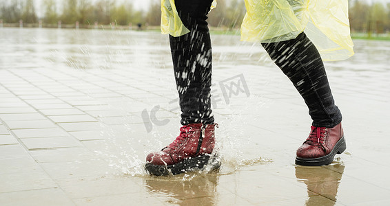 女人在雨中玩耍，在溅起的水坑中跳跃