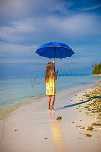 白色沙滩上脚趾撑着雨伞的小女孩