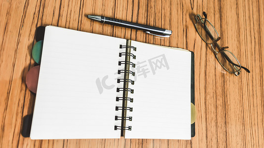 日记页摄影照片_有空白页、眼镜和笔的开放笔记本的书桌。