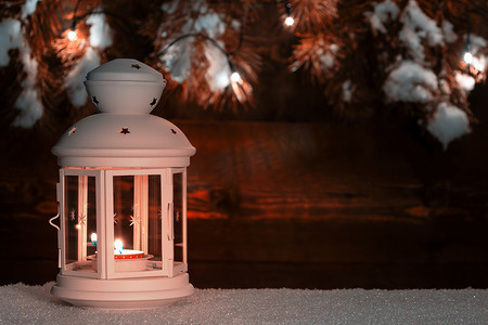 灯笼在雪地上点燃蜡烛，背景是用圣诞树枝和圣诞灯饰装饰的旧木墙。