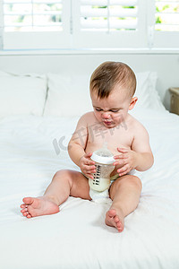 男婴坐在家里床上的牛奶瓶