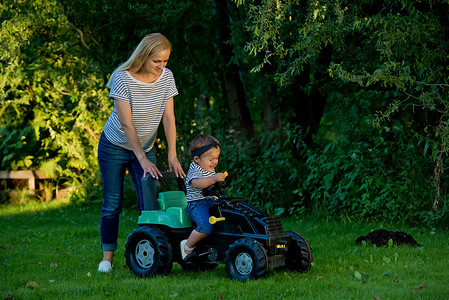 小女孩和妈妈在花园里玩玩具拖拉机。