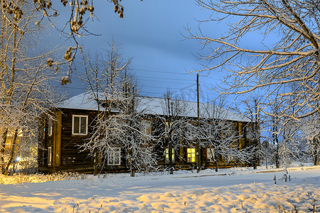 一条多雪的冷淡的街道上的老木房子在夜照明