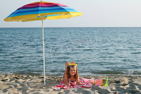 戴着潜水面罩躺在沙滩遮阳伞下的小女孩