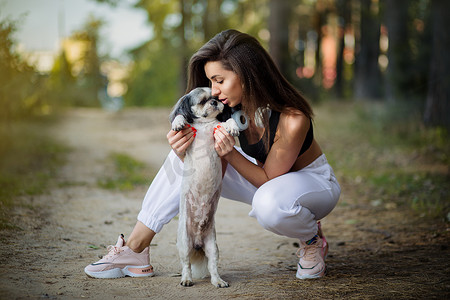 一位年轻女子和她可爱的西施犬坐在树林的小路上。