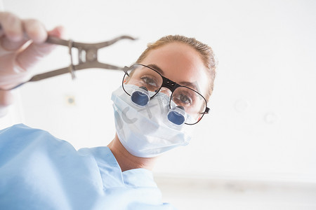 戴外科口罩的牙医和​​牙科放大镜将钳子夹在病人身上
