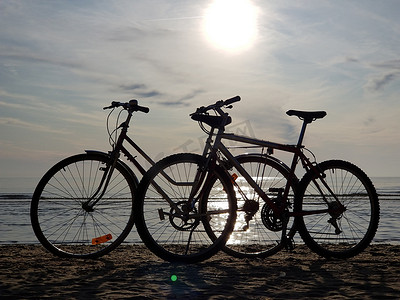 在阳光明媚的夏日，两辆停在沙滩上的自行车现出轮廓