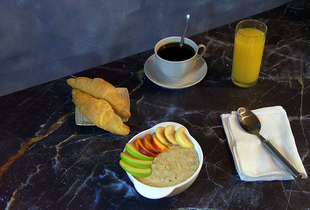 健康早餐、一杯带水果片的燕麦片、一杯橙汁、黑咖啡和两个羊角面包。