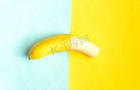 分割线黄色摄影照片_蓝色黄色背景上部分去皮的香蕉。热带夏季水果。