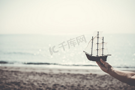 玩具帆船摄影照片_女人在沙滩上拿着船模型
