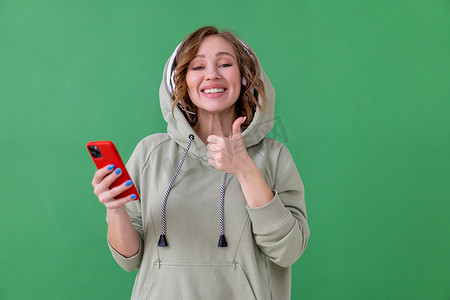 手机绿色背景摄影照片_快乐的牙齿微笑女人听音乐耳机绿色背景 Chromakey 竖起大拇指