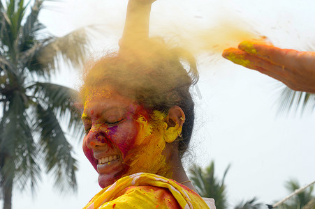 快乐女人节快乐摄影照片_在 Holi 色彩节期间，一位年轻的印度快乐女人的肖像，脸上涂着粉红色、黄色和红色的 Holi 彩色粉末涂料。