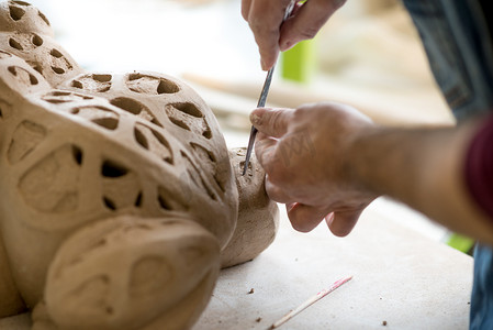 陶艺师穿着围裙在明亮的陶瓷车间用生粘土雕刻雕像。