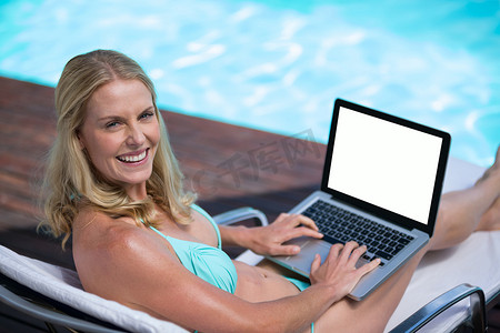 穿着比基尼的美女在游泳池附近使用笔记本电脑