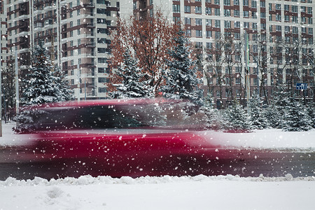一辆行驶中的汽车在雪中的冬季道路上沿着一座高楼行驶