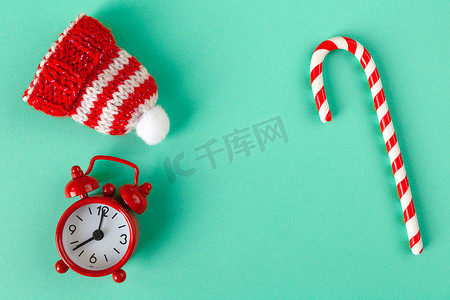 圣诞糖果拐杖摄影照片_圣诞糖果手杖、时钟和帽子在柔和的绿松石背景上，带有复制空间。
