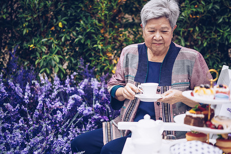 亚洲老年老年妇女在薰衣草花园里喝咖啡茶。