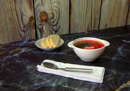 传统的俄罗斯汤罗宋汤配酸奶油和香草，站在桌子上，旁边是盘子里的面包片和带勺子的餐巾纸。