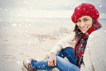沙滩衣服摄影照片_穿着时髦保暖衣服的微笑女人坐在沙滩上