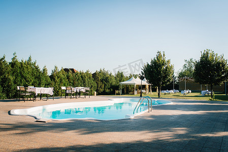 花园游泳池摄影照片_被树木环绕的花园中的蓝色室外游泳池