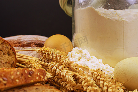 面包、面包片、小麦粉、鸡蛋和木头背景上的谷穗。