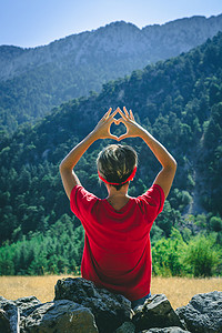 年轻女子坐在山上，用她的双手展示心形。