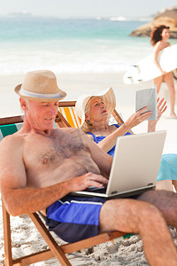 书的海洋摄影照片_男人在笔记本电脑上工作，而他的妻子在沙滩上看书