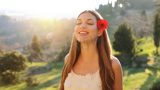 美丽的年轻女子，留着长头发，耳朵上挂着红色的花，在大自然中呼吸新鲜空气。