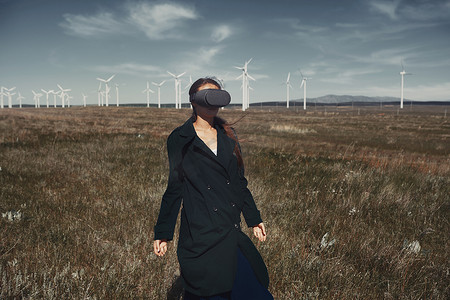 在风力涡轮机旁边的田野里戴着 VR 耳机的女人
