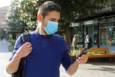 COVID-19 大流行冠状病毒年轻人戴着外科口罩在城市街道使用智能手机应用程序帮助接触者追踪和自我诊断以应对 2019 年冠状病毒大流行