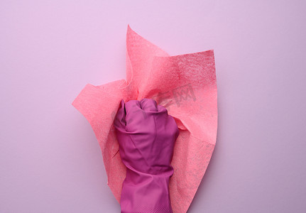 紫色女摄影照片_粉色橡胶手套中的女手拿着紫色背景上的粉色清洁抹布