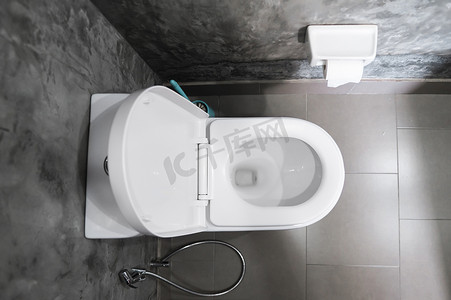 家庭浴室白色马桶上的白色悬挂式马桶座，墙上铺着混凝土风格的灰色瓷砖和卫生纸。