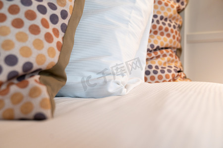 卧室床边摄影照片_卧室新铺的床上铺着红色黄色和灰色点缀的散布靠垫和白色睡枕。