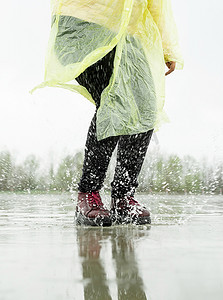 人在雨中摄影照片_女人在雨中玩耍，在溅起的水坑中跳跃
