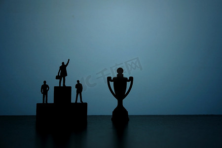 商业战略概念照片-微型商人站在领奖台上指着奖杯的剪影