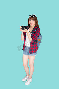 微笑的美丽年轻亚洲女性是记者摄影师穿着时尚旅行夏季，女孩拿着相机爱好旅游和度假旅行，在蓝色背景下孤立。