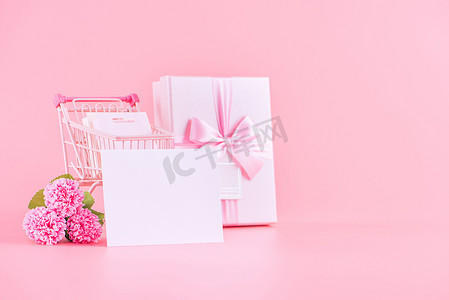 母亲节康乃馨摄影照片_购物车和康乃馨在粉红色的桌子背景上的礼物。