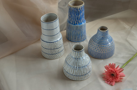四个蓝色和白色手工陶瓷花瓶，粉色花朵装饰在腮红纹理桌布上。