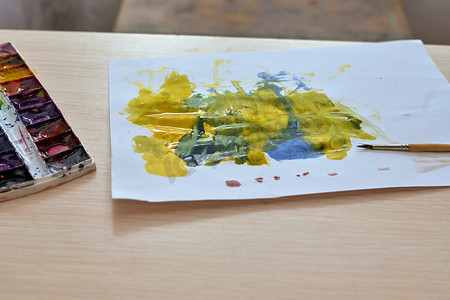 用水彩画的孩子躺在桌子上，纸上有彩色斑点