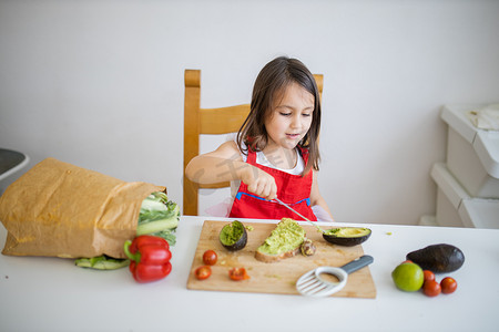 餐桌旁的小女孩在一片面包上撒鳄梨