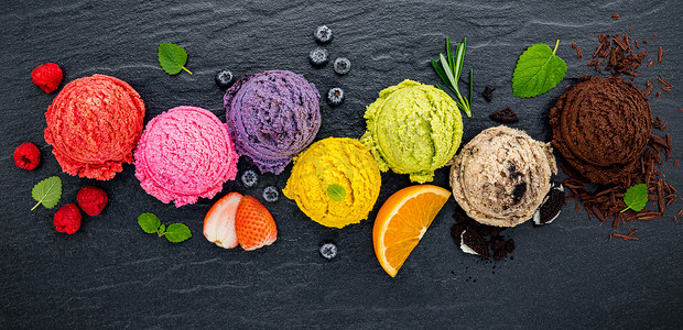 各种冰淇淋风味球蓝莓、酸橙、开心果、杏仁、橙子、巧克力和香草在深色石头背景上设置。