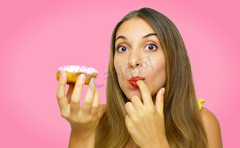 贪婪的女孩在粉红色的背景下抓着甜甜圈准备吃。