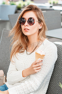 坐在夏季咖啡馆里的圆形太阳镜和冰淇淋的时尚漂亮女孩。