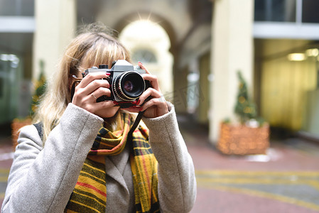 金发美女摄影师手里拿着复古相机，同时在城市旧建筑上拍照。