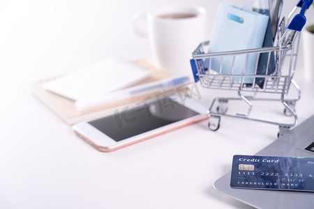 办公室在线支付、在家购物、带信用卡概念的电子支付、带购物车的白桌背景笔记本电脑、特写。