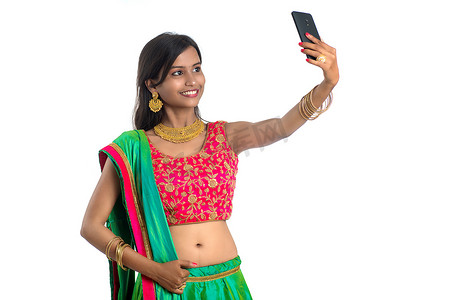 年轻的印度女孩使用手机或智能手机，在白色背景下自拍或视频聊天