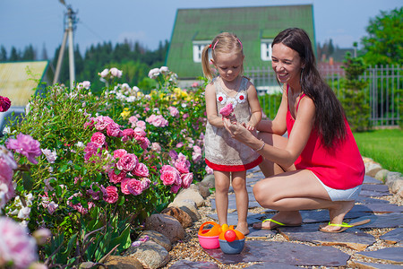 年轻的母亲和她可爱的女儿在花园里的花边